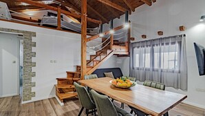 A dining area with a wooden table, green upholstered chairs, a fruit bowl, a staircase with a rope railing, and a TV mounted on the wall. - Villa Sea Edge (Orebic)