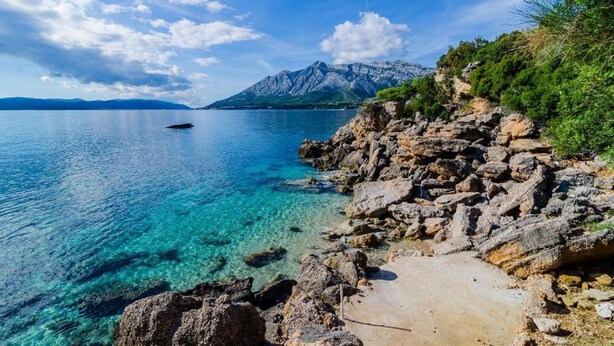 A rocky shoreline with clear blue water and a mountain in the background. - Villa Sea Edge (Orebic)