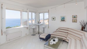 A bright, modern room with large windows, a glass coffee table, a striped sofa, and a small bar area. - Apartment Rea (Dubrovnik)