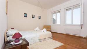 A bedroom with a bed, bedside table, lamp, and a large window. - Apartment Rea (Dubrovnik)