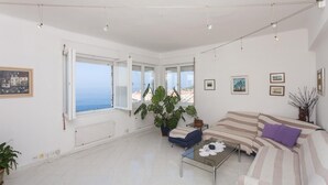A bright living room with a large window, a sofa, a coffee table, and a potted plant. - Apartment Rea (Dubrovnik)