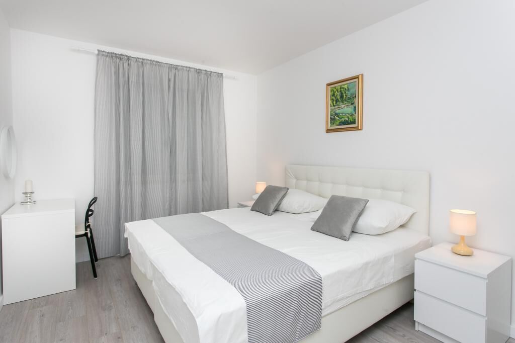 A modern bedroom with a large bed, a desk, and a nightstand.