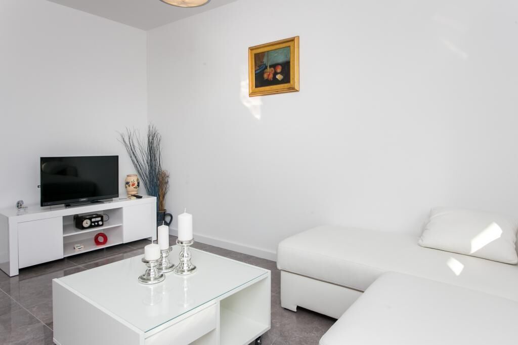A modern living room with a flat-screen TV, white sofa, glass coffee table, and a framed picture on the wall.