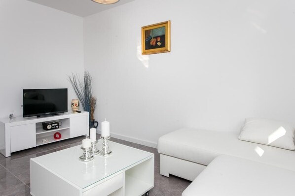 A modern living room with a flat-screen TV, white sofa, glass coffee table, and a framed picture on the wall. - Apartment Dupčić (Dubrovnik)