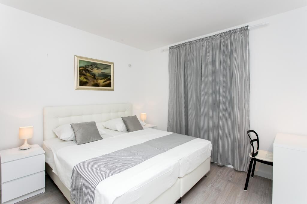 Une chambre à coucher bien rangée, avec un lit, des tables de chevet, une chaise et un tableau accroché au mur.