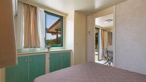 Une chambre à coucher avec un lit, une fenêtre avec des rideaux, une armoire verte et une vue sur l’extérieur.