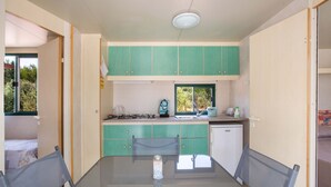 Une cuisine compacte avec des meubles de couleur turquoise, une cuisinière à gaz, un évier et un petit réfrigérateur.