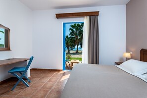A hotel room with a bed, desk, chair, and a view of the beach. - Olympia Mare  (Kos)