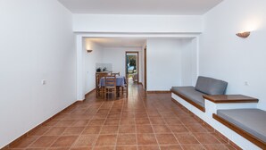 A spacious room with a tiled floor, a sofa, a dining table with chairs, and a kitchen area in the background. - Olympia Mare (Kos)