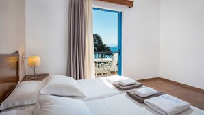 A hotel room with two beds, a nightstand with a lamp, a view of the balcony, and a table with chairs outside. - Olympia Mare (Kos)