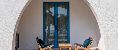 A small patio with two wooden chairs and a table, a blue-framed door, and a white textured wall.