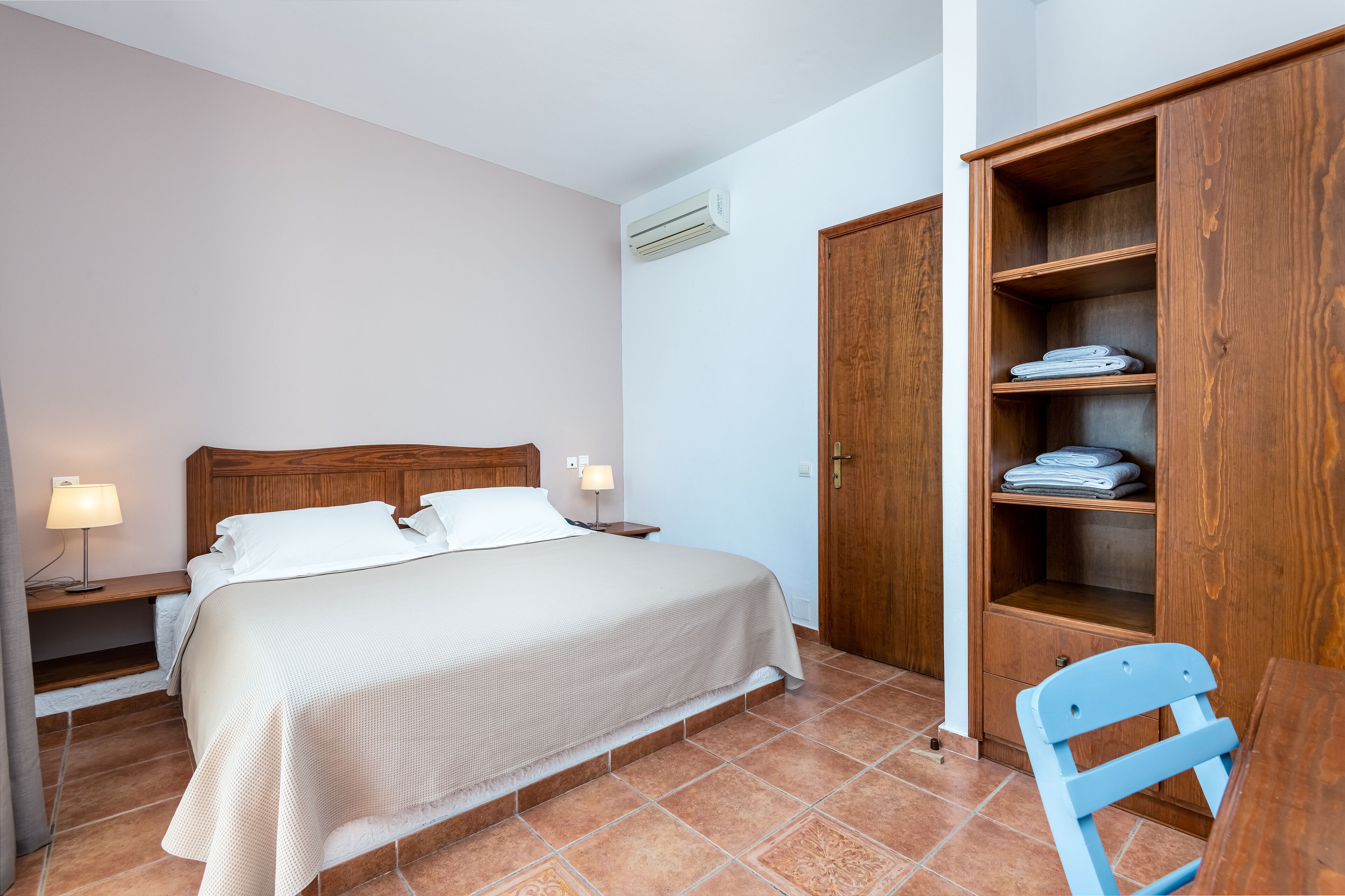 A bedroom with a bed, bedside lamps, a wooden wardrobe, and a chair.