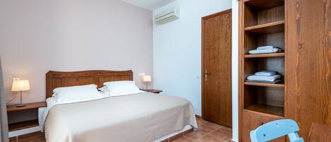 A bedroom with a bed, bedside lamps, a wooden wardrobe, and a chair.