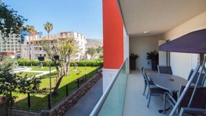 A balcony with a dining table and chairs, overlooking a well-maintained garden and buildings in the background. - Apartment Vesna (Dubrovnik)