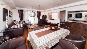 A modern living room with a dining area, featuring a striped tablecloth, brown leather chairs, and a hanging light fixture. - Apartment Vesna (Dubrovnik)
