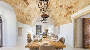 A dining room with a long wooden table set for a meal, surrounded by chairs. The room features exposed brick walls and a high ceiling with a decorative metal fixture. - 2874 Masseria Marchese by Perle di Puglia (Montesano Salentino)