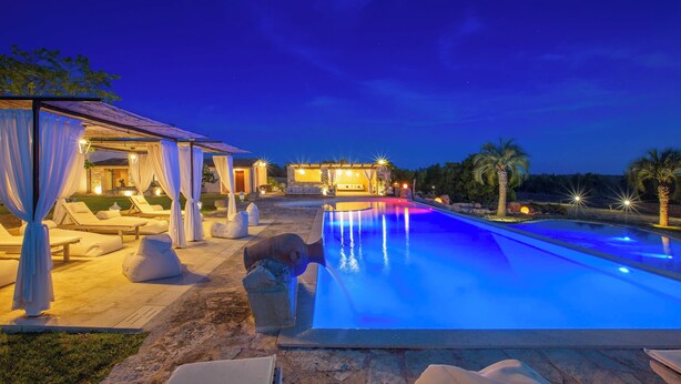 A pool with a water feature, lounge chairs, and a covered seating area at dusk. - 2874 Masseria Marchese by Perle di Puglia (Montesano Salentino)