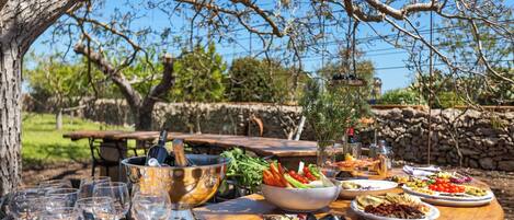 Una mesa de comedor al aire libre con varios platos, copas y una botella de vino.