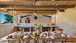 An outdoor dining area with a wooden table set for a meal, surrounded by chairs, and a rustic ceiling with hanging light fixtures. - 2874 Masseria Marchese by Perle di Puglia (Montesano Salentino)
