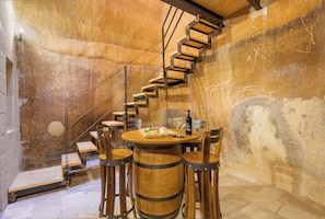 A rustic interior with a wooden spiral staircase, a round wooden table with chairs, and a bottle of wine.