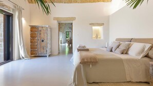 A bedroom with a large bed, a wooden cabinet, and a stone archway leading to another room. - 2874 Masseria Marchese by Perle di Puglia (Montesano Salentino)
