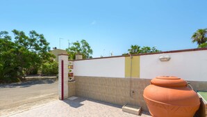A tiled patio area with a large terracotta pot, a wall with a door, and a clear sky. - 3033 Villetta Angela by Barbarhouse (Melendugno)