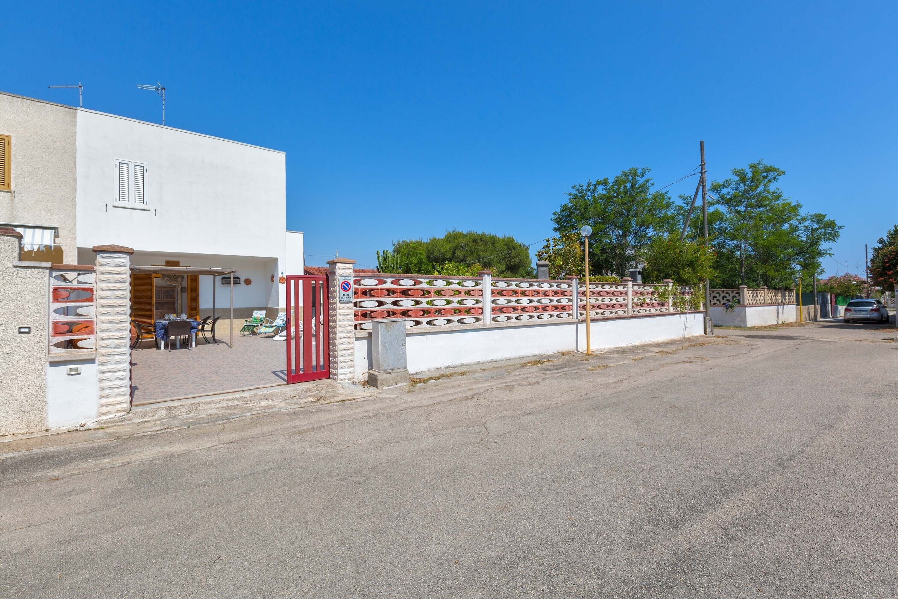 A modern building with a white facade, a red gate, and a paved entrance area with outdoor seating.