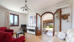 A living room with a TV, red and white sofas, a coffee table, and a glass cabinet. There is a large window and an open door leading to a patio. - 2989 Villetta Mito - Mito A by Barbarhouse (Tricase)