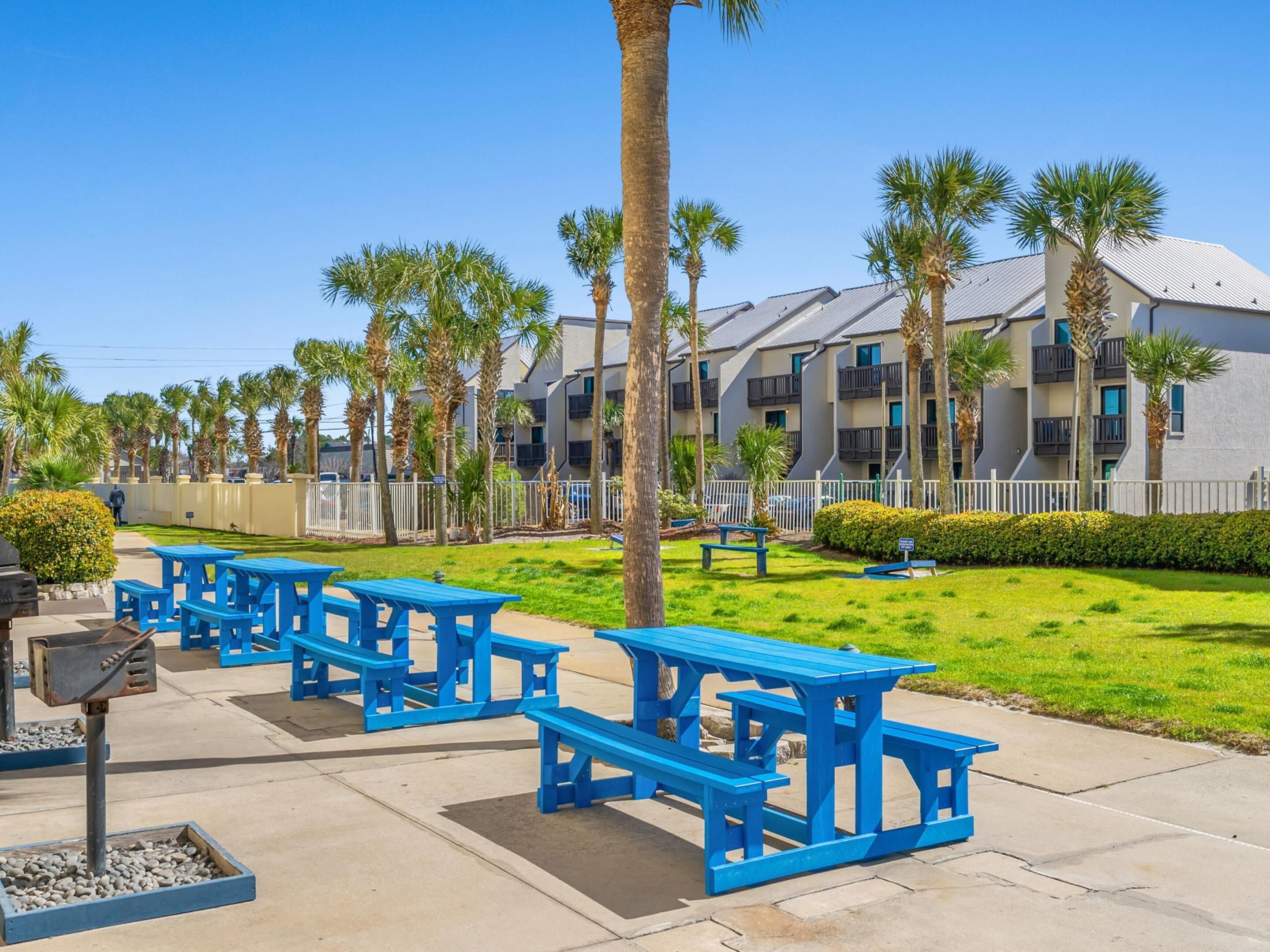 A courtyard with blue picnic tables, palm trees, and a row of apartment buildings.