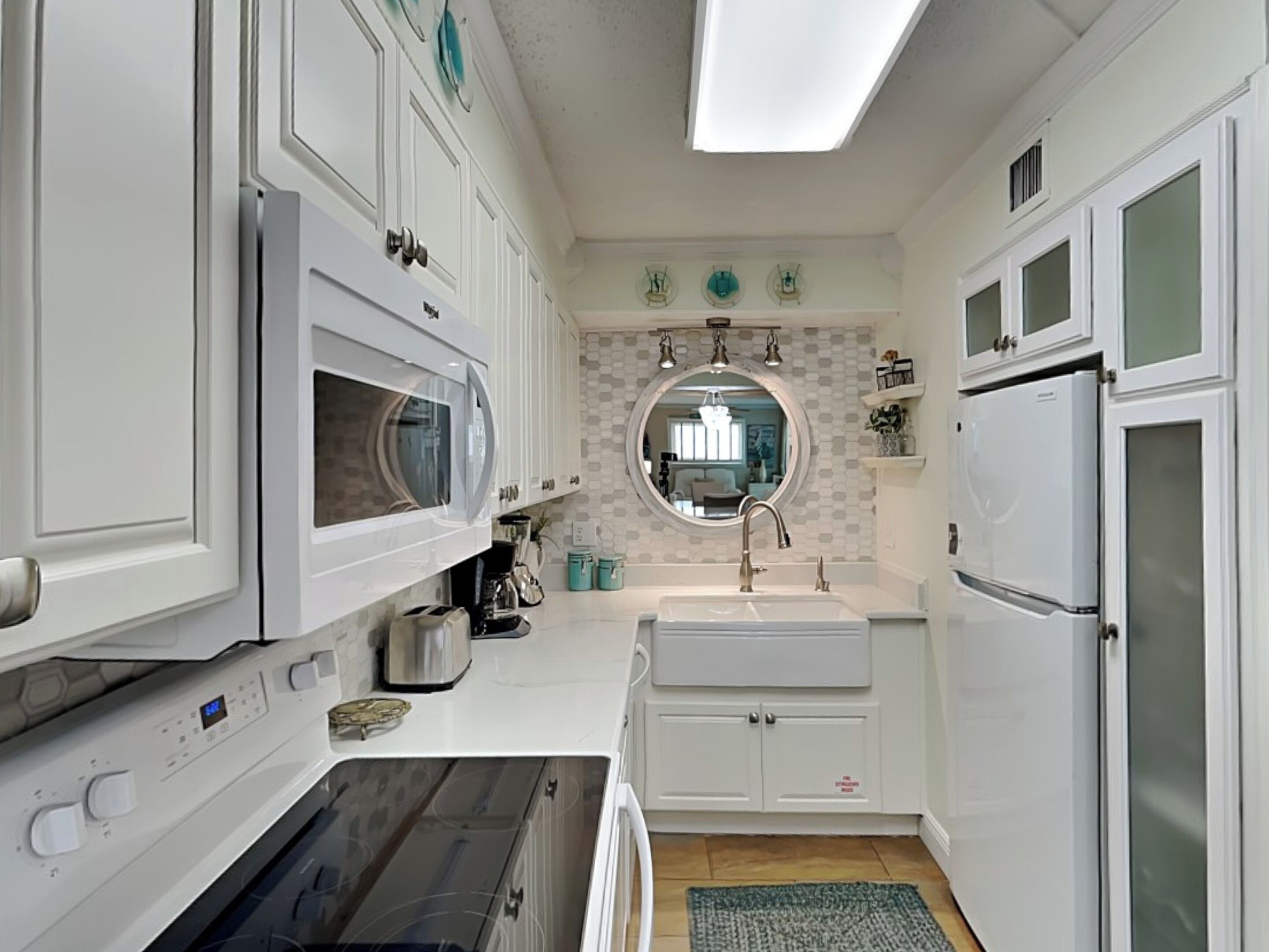 A compact kitchen with white cabinets, a microwave, a stove, a sink, and a refrigerator.
