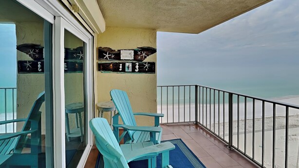 Ein Balkon mit türkisfarbenen Stühlen und einem Tisch mit Blick auf einen Strand.