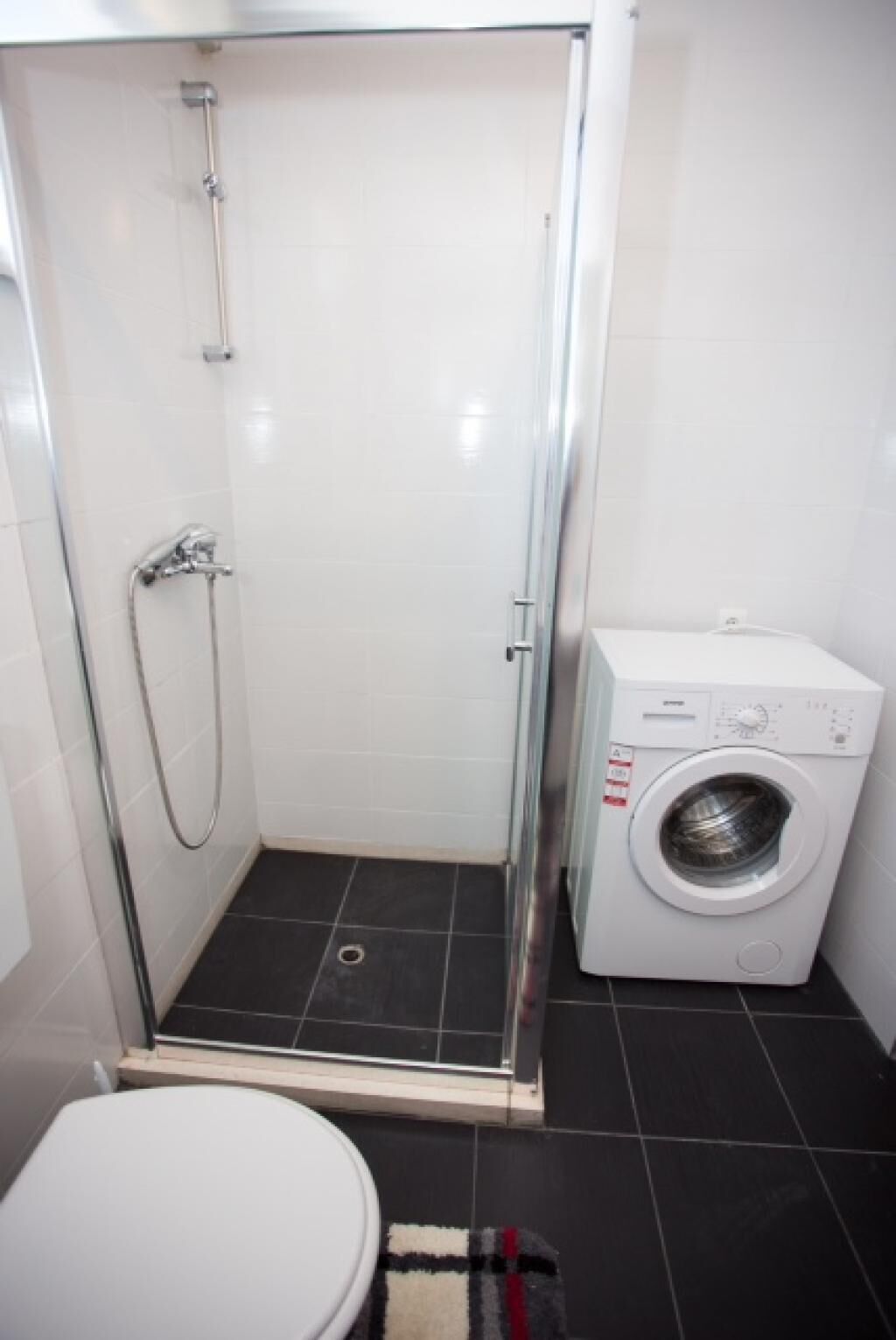 A small bathroom with a shower, toilet, and a washing machine.