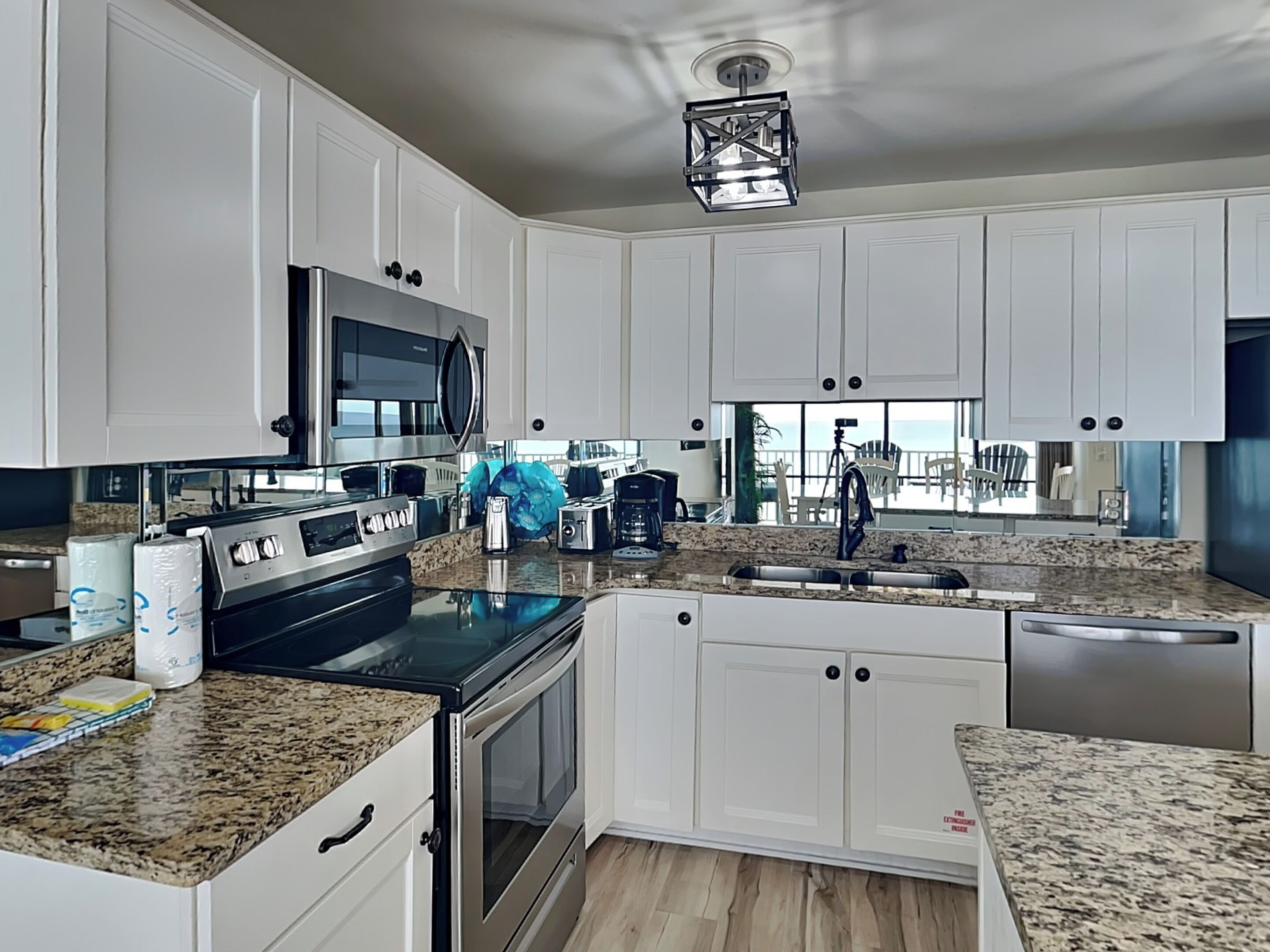 A modern kitchen with white cabinets, granite countertops, stainless steel appliances, and a large window offering a view of the outdoors.