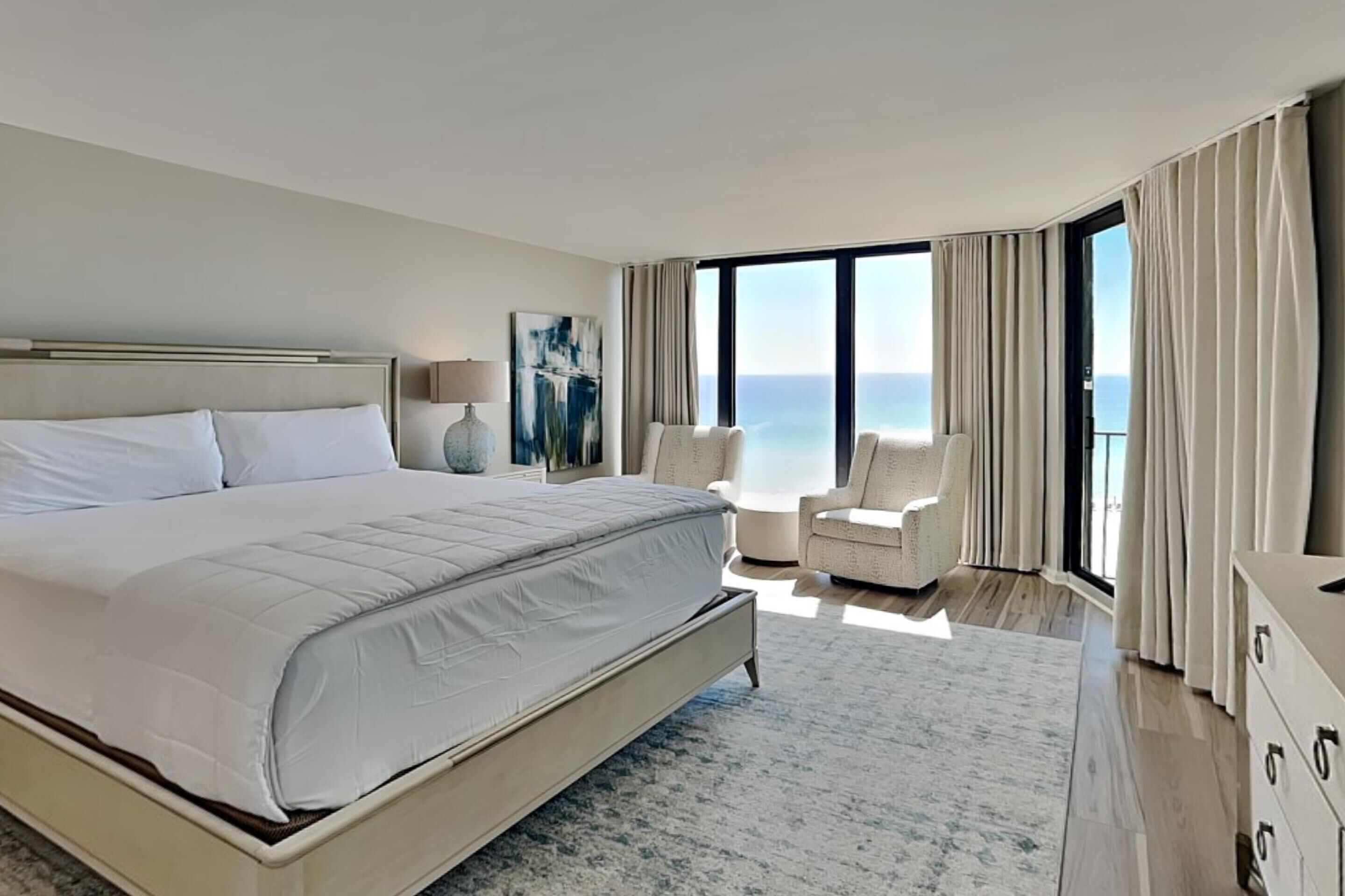 Un dormitorio moderno con una cama grande, una silla y vistas al océano.