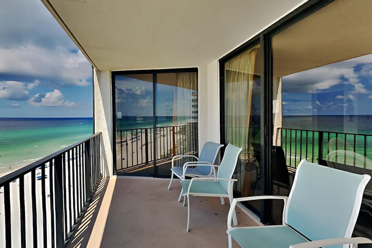 A balcony with a view of the ocean and beach, featuring two chairs and a table.