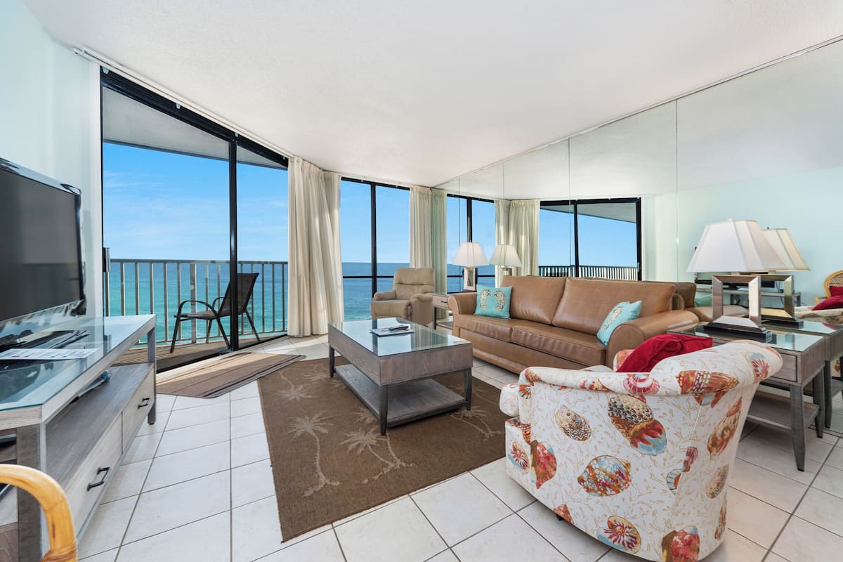 A spacious living room with a large window, a sofa, a coffee table, a TV, and a dining area with chairs.
