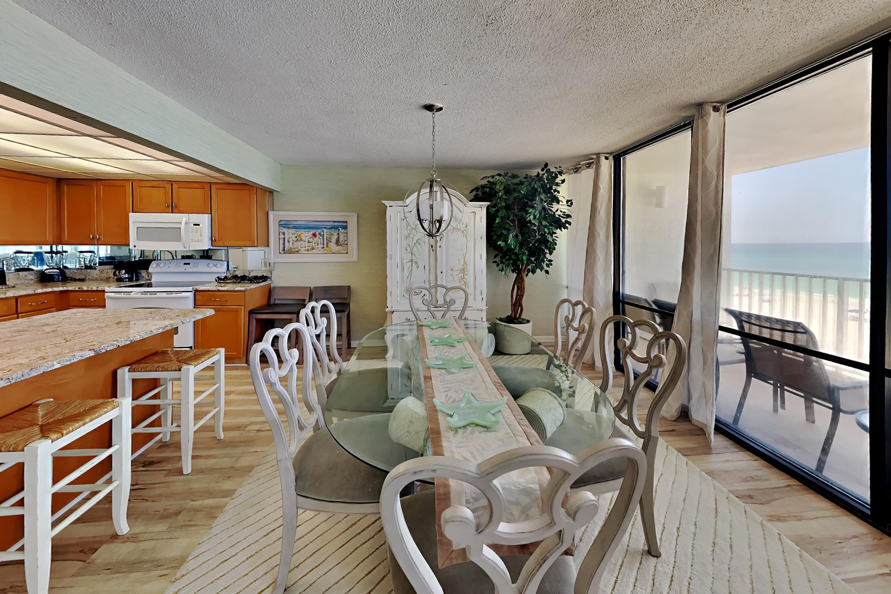 A modern kitchen with a central island, a dining area with a glass table, and a view of the ocean.