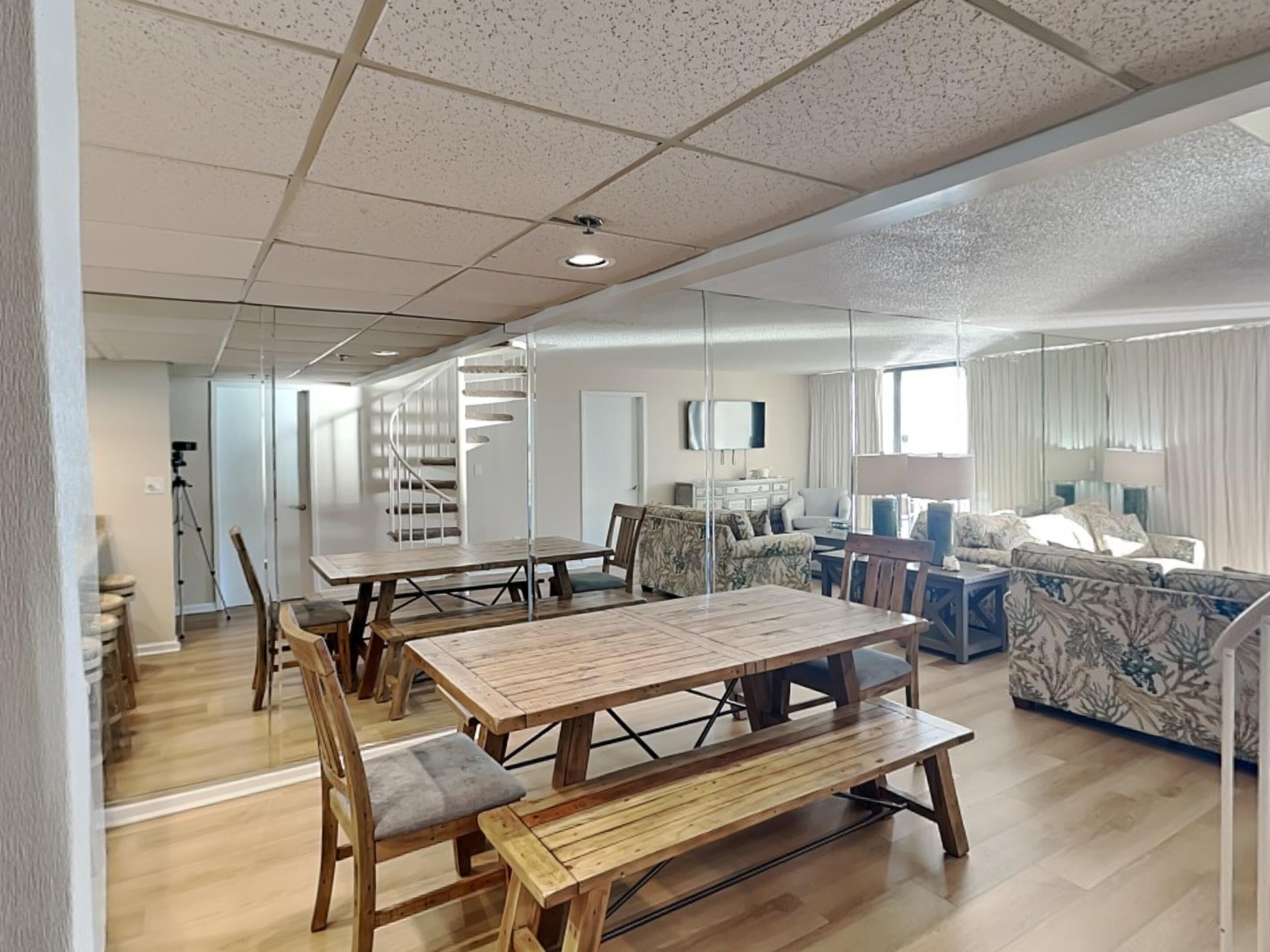 A spacious living area with a wooden dining table and benches, a staircase, and a seating area with patterned sofas.