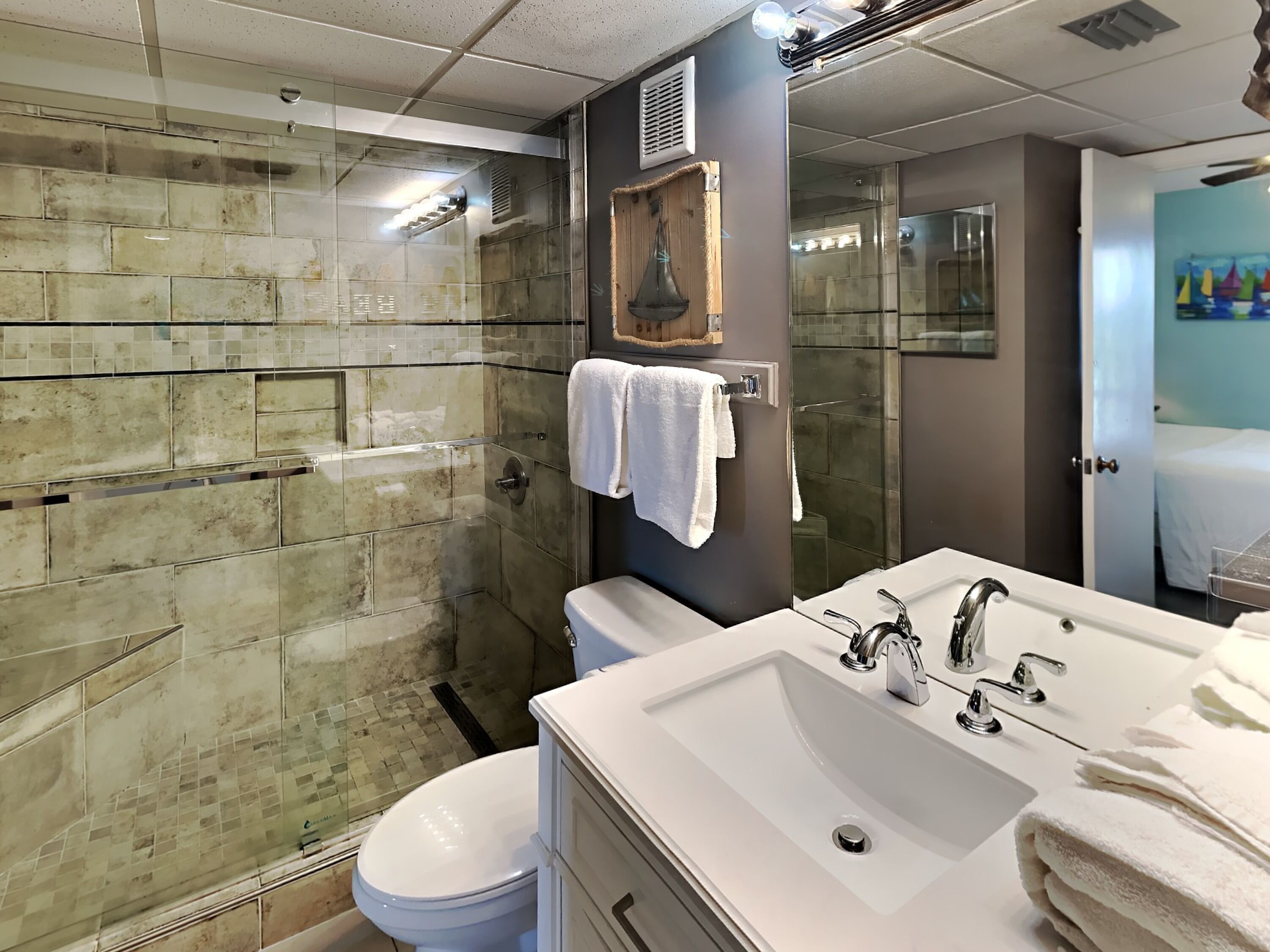 A modern bathroom with a glass shower enclosure, a white toilet, a large sink with a mirror, and a towel rack.