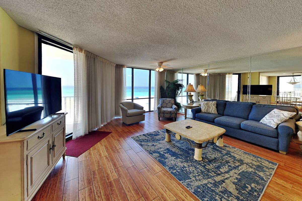 A spacious living room with a large TV, comfortable seating, a coffee table, and a view of the ocean.