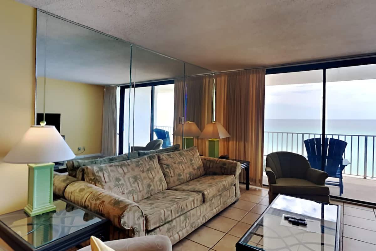 A living room with a sofa, armchairs, a glass coffee table, and a view of the ocean.