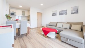 A modern living room with a grey sofa, a dining table with chairs, and a kitchen in the background. - Apartment Luce Royal (Dubrovnik)