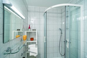 Uma casa de banho moderna com cabine de chuveiro em vidro, prateleira de vidro com artigos de higiene e porta-toalhas branco.