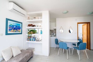 Uma sala de estar moderna com sofá, mesa de jantar com cadeiras, cozinha e corredor que leva a uma porta.