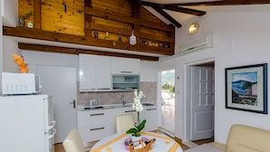 A compact kitchen with white cabinets, a microwave, and a sink. There's a dining area with a table set for two, a chair, and a sofa. A framed picture is on the wall, and a window reveals a view of the outdoors. - Apartment Marina View (Dubrovnik)