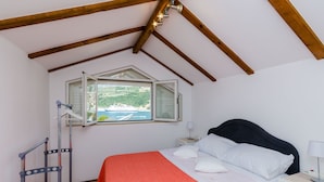A bedroom with a bed, a nightstand, a window with a view of a body of water, and a wooden ceiling. - Apartment Marina View (Dubrovnik)