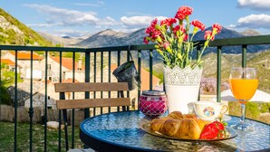 A table with croissants, strawberries, a glass of orange juice, a teacup, and a vase of flowers on a balcony with a mountain view. - Country Home Matkovic - Duba (Konavle)