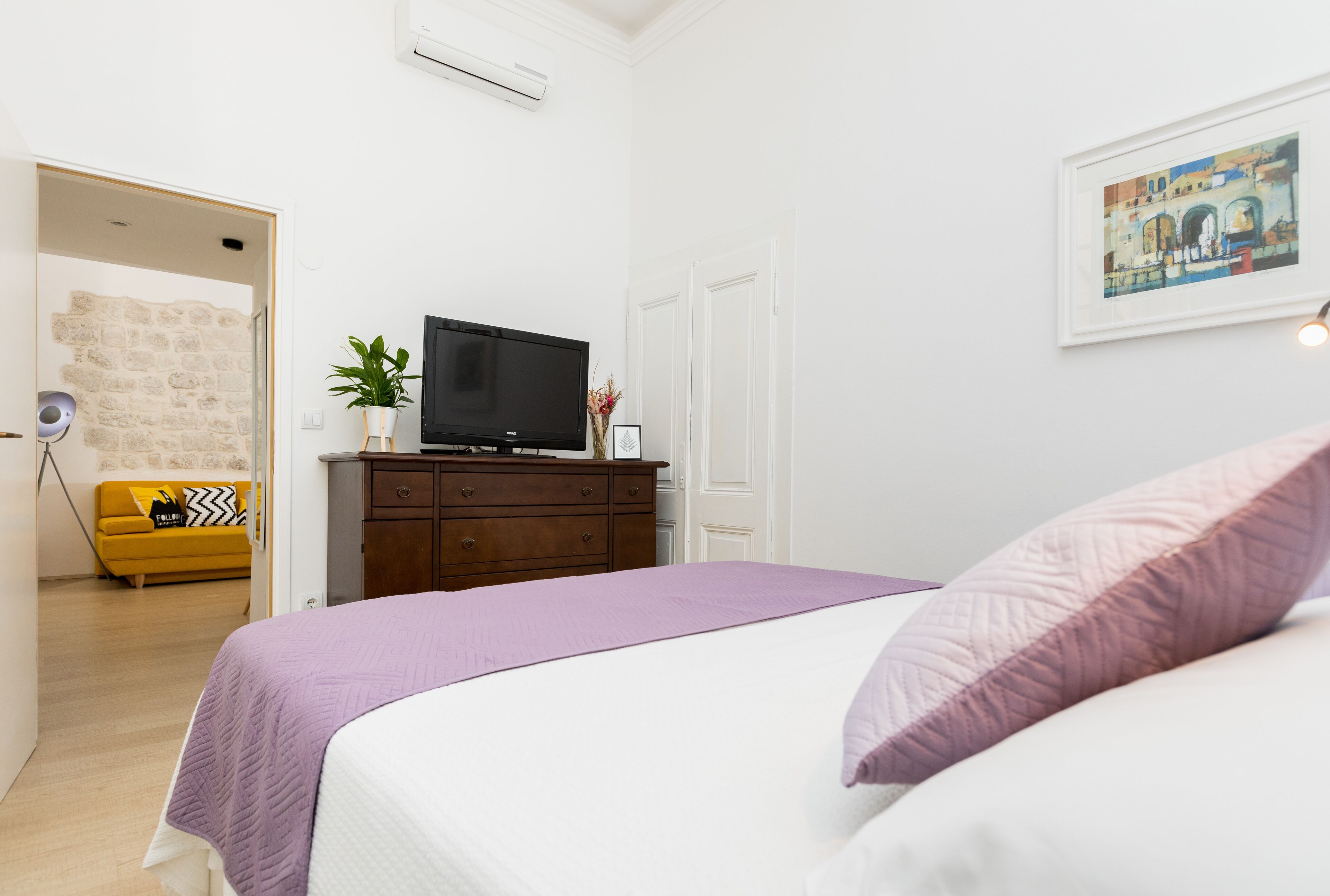 A bedroom with a bed, a dresser, a television, and a painting on the wall.