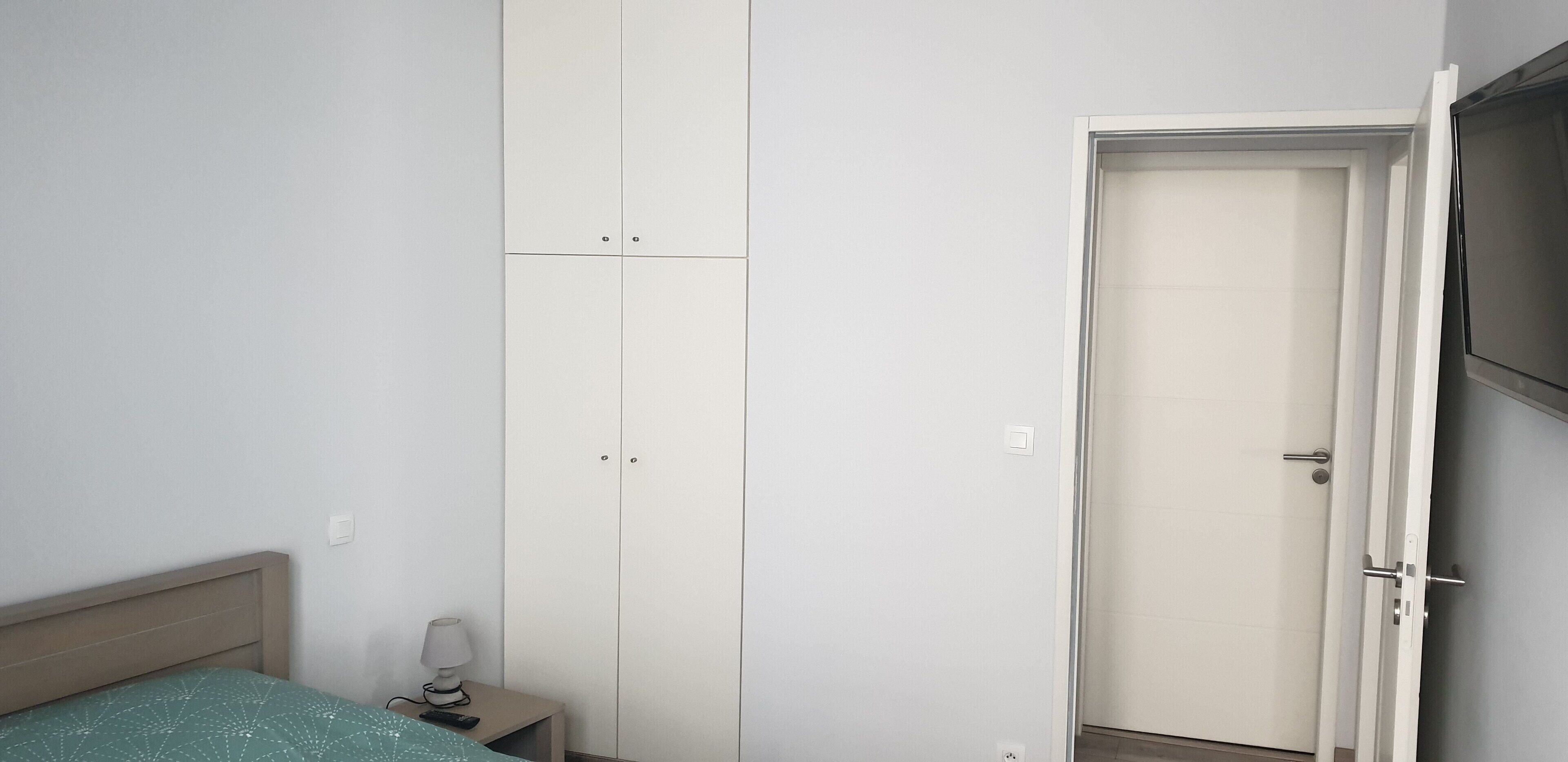 Un dormitorio con cama, mesita de noche, armario y una puerta que da a otra habitación.