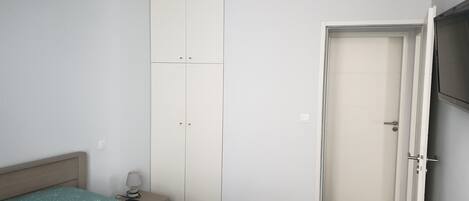 Un dormitorio con cama, mesita de noche, armario y una puerta que da a otra habitación.